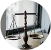 A close-up shot of a traditional bronze scale of justice on a wooden surface, with a blurred background of an office or courtroom.