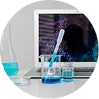 A laboratory scene with a laptop displaying a digital pattern, a beaker with a stirring rod, a flask with blue liquid, and other scientific glassware on a white surface