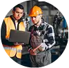 "Two industrial workers wearing safety helmets and reflective vests discussing a clipboard in a factory or industrial setting."