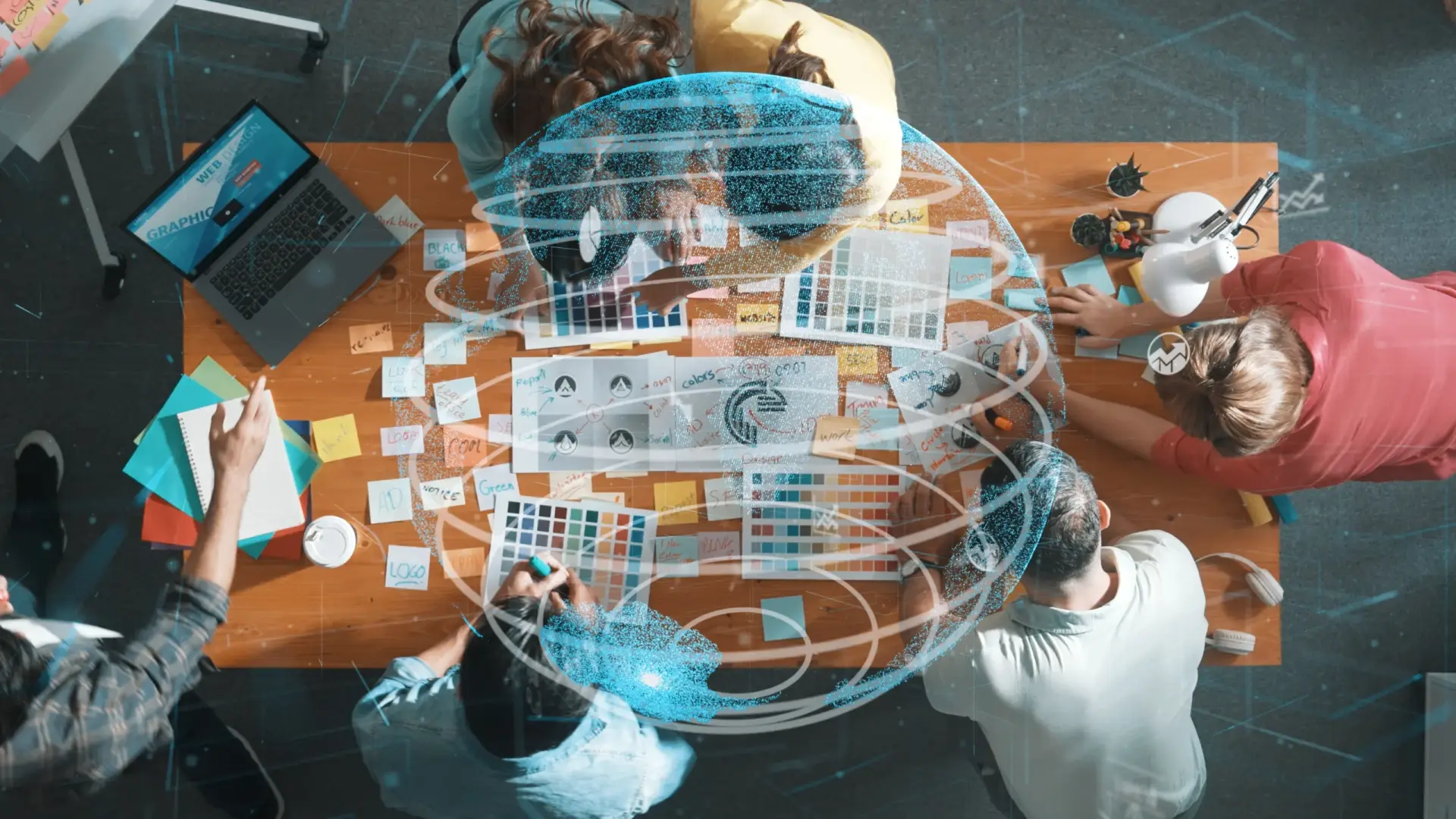 A group of people collaborate at a table covered with color swatches, sketches, and sticky notes, with a laptop open, overlaid by a digital globe graphic
